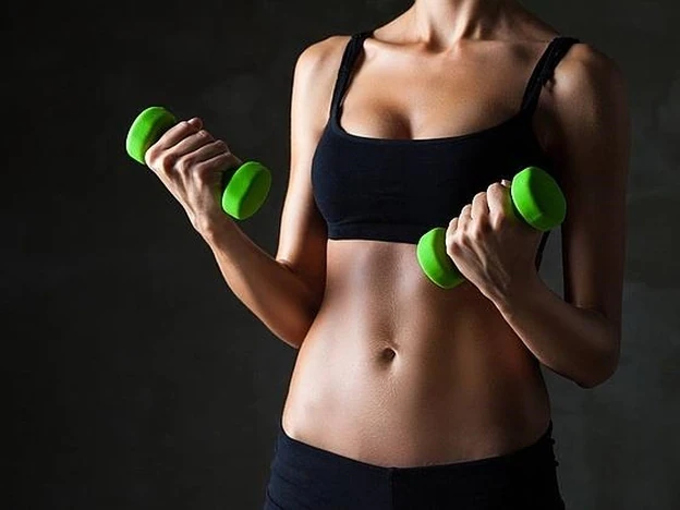 Una mujer sostiene unas mancuernas tras practicar ejercicio en el gimnasio./