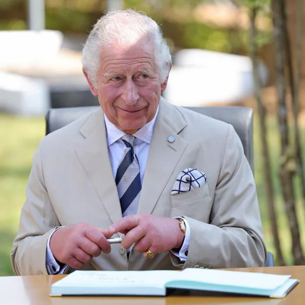 El rey británico Carlos III sonríe con un bolígrafo en la mano.