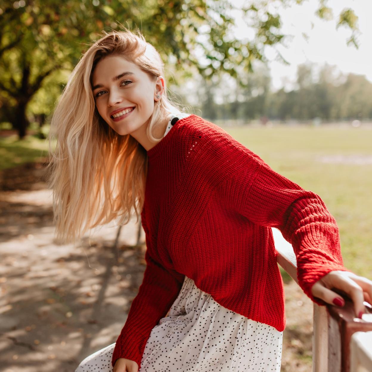 Mujer de pelo largo y rubio sonriendo en un parque. /Imagen de lookstudio en Freepik.