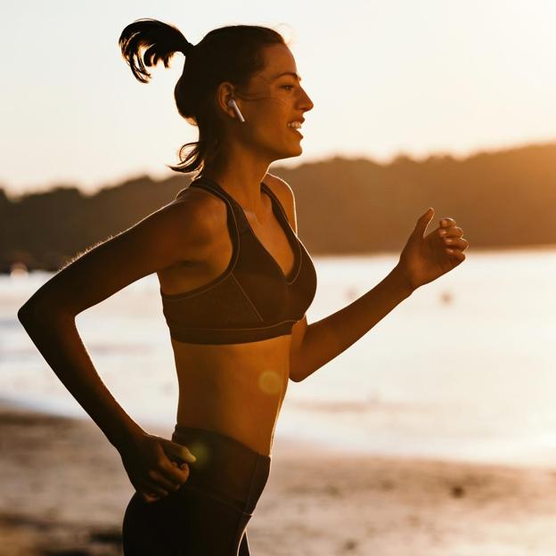 Mujer realizando running en la playa al amanecer. 