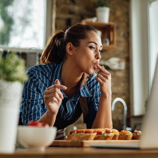 Mujer comiendo mientras de pie sobre la barra de la cocina. 