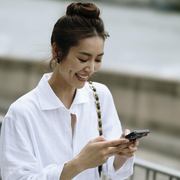 Una mujer con camisa blanca consultando el móvil.