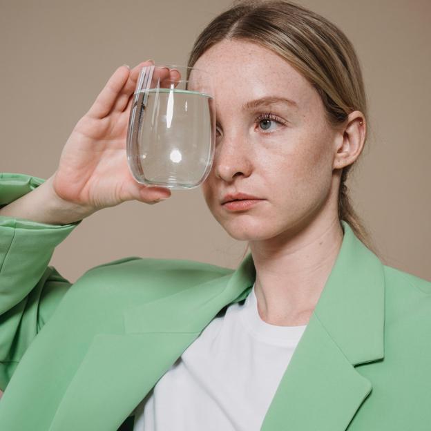 Mujer con chaqueta verde y vaso de agua.