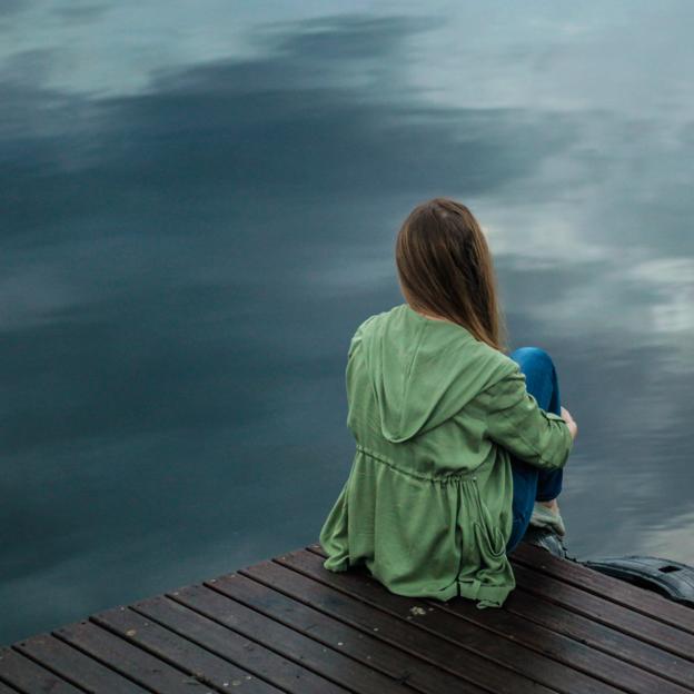 Mujer sentada en un muelle mirando al mar. 