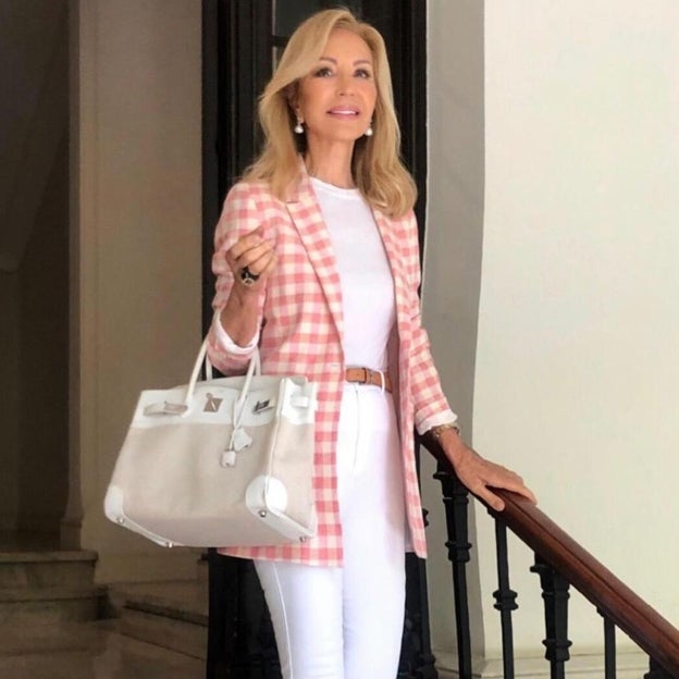 Carmen Lomana con un look de chaqueta de tweed, perlas y bolso clásico combinados con jean pitillo de color blanco.