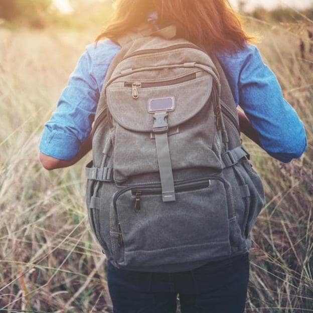 Mujer caminando por el campo con una mochila a la espalda. 